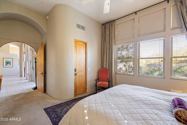 bedroom with ceiling fan, light carpet, and a high ceiling