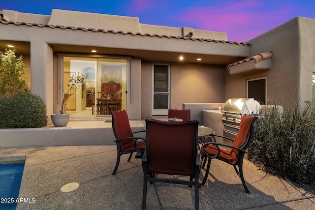 patio terrace at dusk with an outdoor kitchen and a grill