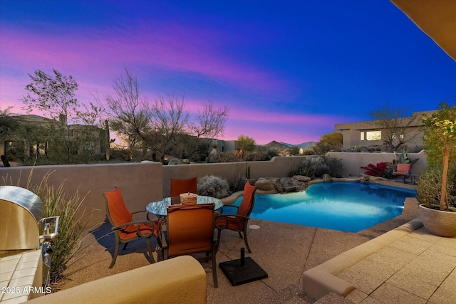 pool at dusk with area for grilling, grilling area, and a patio area