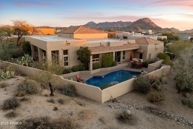 back house at dusk with a fenced in pool, a patio, and a mountain view