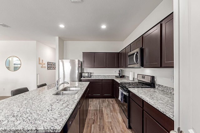 5875 N 195th Dr, Litchfield Park, AZ 85340 - kitchen featuring appliances with stainless steel finishes, light wood-style floors, a sink, an island with sink, and dark brown cabinets