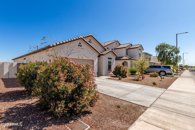 mediterranean / spanish house featuring a garage, concrete driveway, a tile roof, and stucco siding