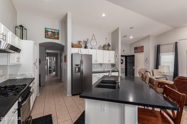 kitchen featuring arched walkways, stainless steel appliances, dark countertops, and a sink