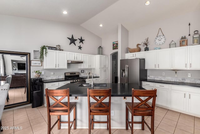 kitchen featuring arched walkways, under cabinet range hood, stainless steel appliances, a sink, and dark countertops