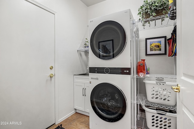 clothes washing area with light tile patterned flooring, cabinets, and stacked washing maching and dryer