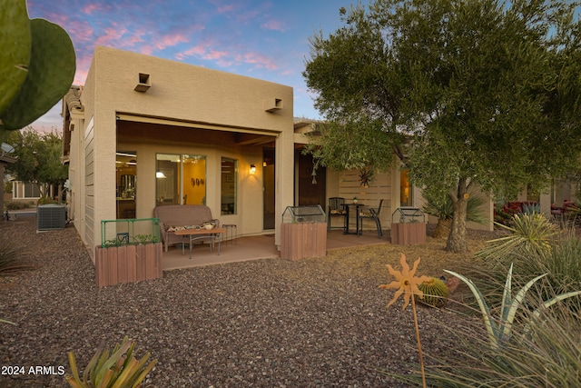 back house at dusk with central AC unit and a patio