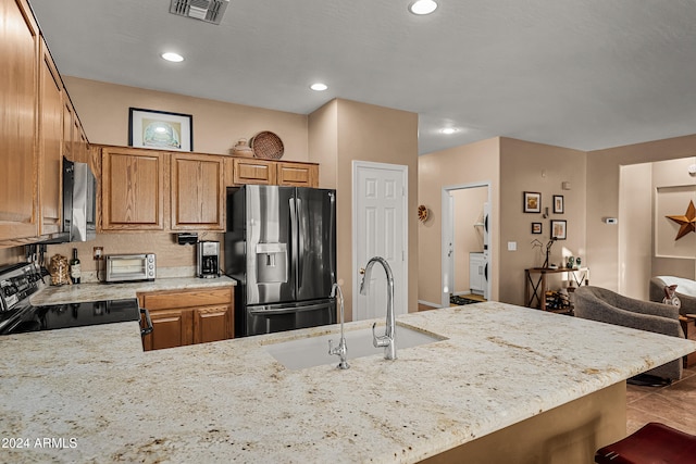 kitchen with a kitchen breakfast bar, sink, light stone countertops, stainless steel appliances, and washer / clothes dryer