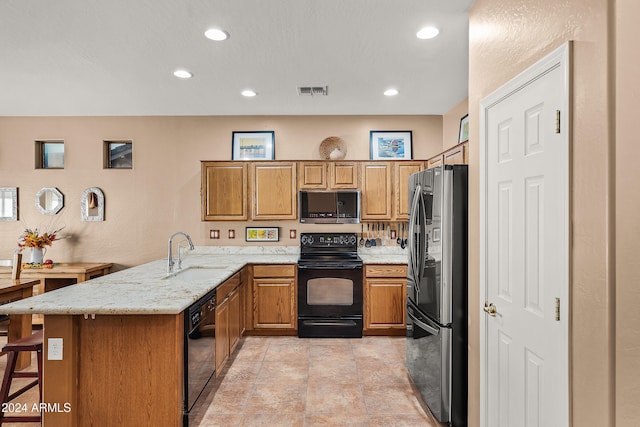 kitchen featuring sink, a kitchen breakfast bar, light stone counters, kitchen peninsula, and black appliances