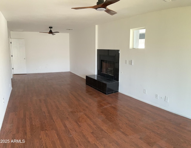 unfurnished living room with ceiling fan, dark wood-style flooring, and a tile fireplace