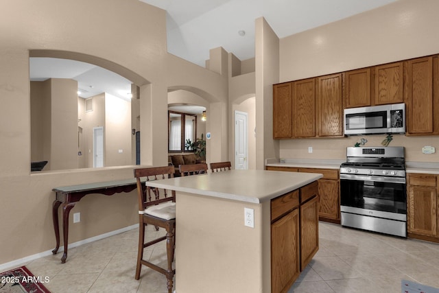 kitchen featuring a towering ceiling, appliances with stainless steel finishes, a breakfast bar area, and a kitchen island