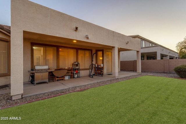 back house at dusk featuring a patio area and a lawn