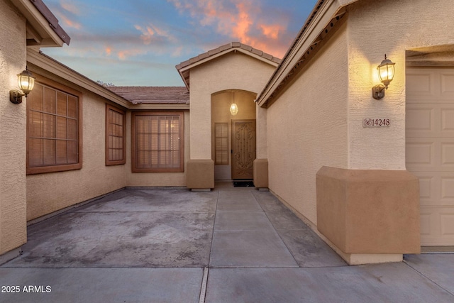 exterior entry at dusk featuring a garage and a patio area