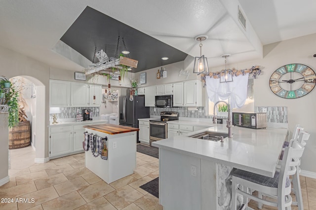 kitchen featuring stainless steel appliances, white cabinets, kitchen peninsula, and wooden counters