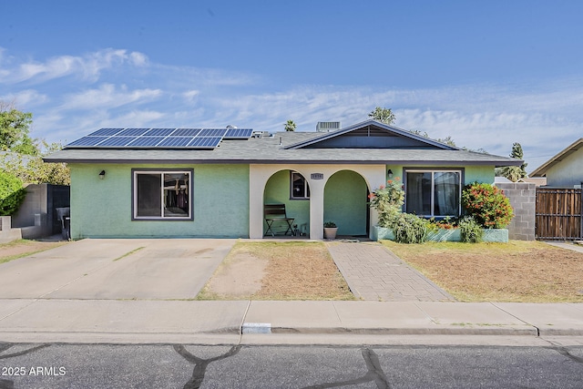 ranch-style house with roof mounted solar panels, stucco siding, a porch, and fence
