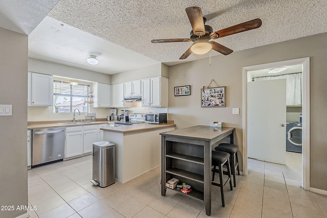 kitchen featuring stainless steel appliances, a sink, range hood, white cabinetry, and washer / dryer