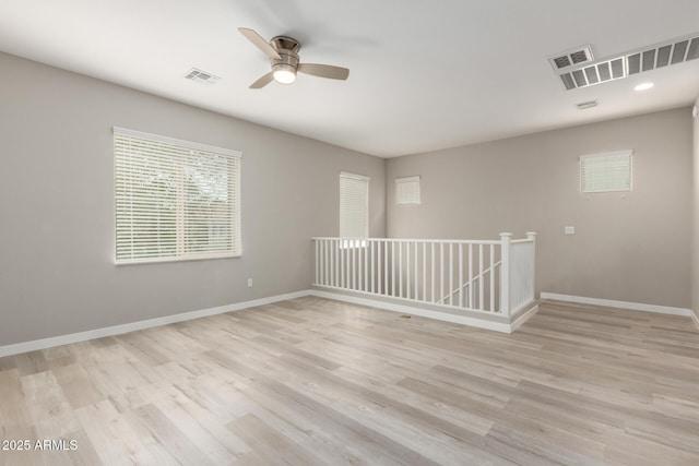 spare room featuring visible vents, light wood-style flooring, a ceiling fan, and baseboards