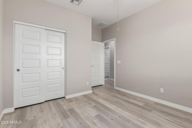 unfurnished bedroom with baseboards, visible vents, attic access, a closet, and light wood-type flooring