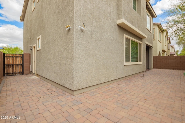 view of property exterior featuring a patio area, stucco siding, a gate, and fence