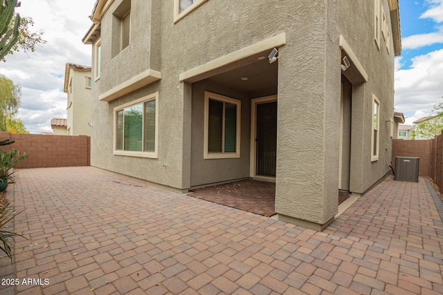 rear view of property with central AC, a patio area, a fenced backyard, and stucco siding