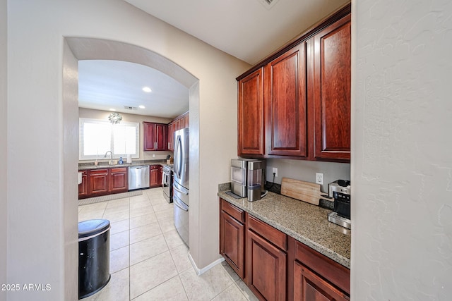 2886 E Hazeltine Way, Chandler, AZ 85249 - kitchen featuring light stone countertops, baseboards, arched walkways, light tile patterned floors, and stainless steel appliances