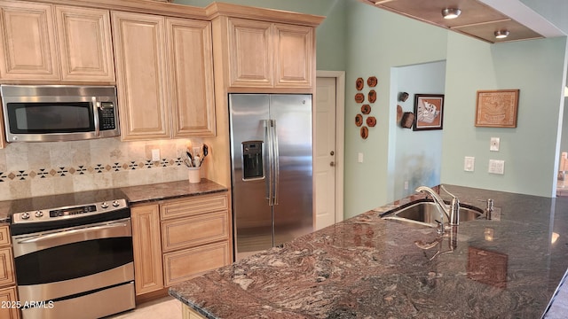 kitchen featuring light brown cabinetry, sink, tasteful backsplash, dark stone countertops, and stainless steel appliances