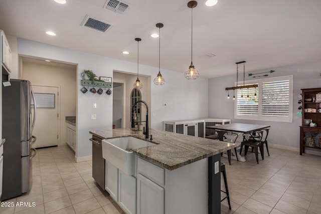 kitchen featuring hanging light fixtures, stainless steel appliances, a kitchen island with sink, dark stone countertops, and sink