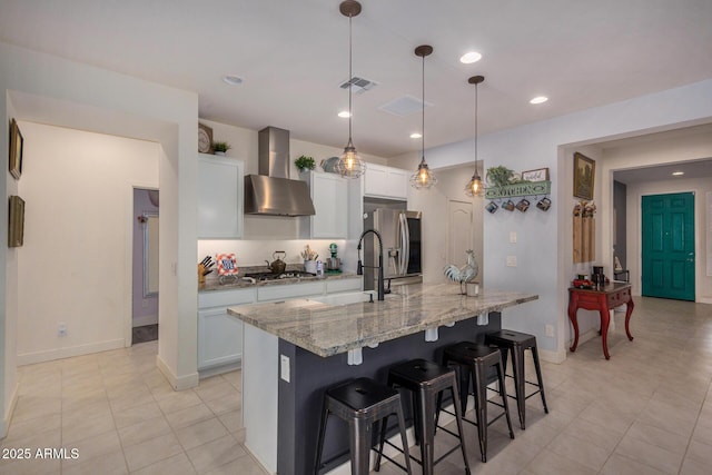 kitchen with appliances with stainless steel finishes, a spacious island, white cabinetry, wall chimney range hood, and decorative light fixtures