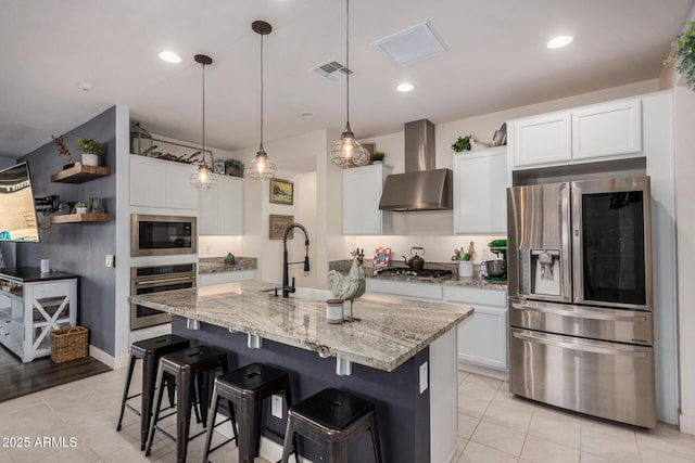 kitchen with stainless steel appliances, pendant lighting, wall chimney exhaust hood, sink, and white cabinetry