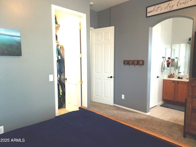 bedroom with arched walkways, a walk in closet, connected bathroom, light tile patterned flooring, and light carpet