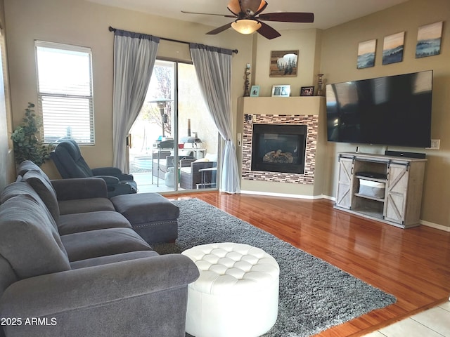 living area featuring wood finished floors, ceiling fan, a tiled fireplace, and baseboards