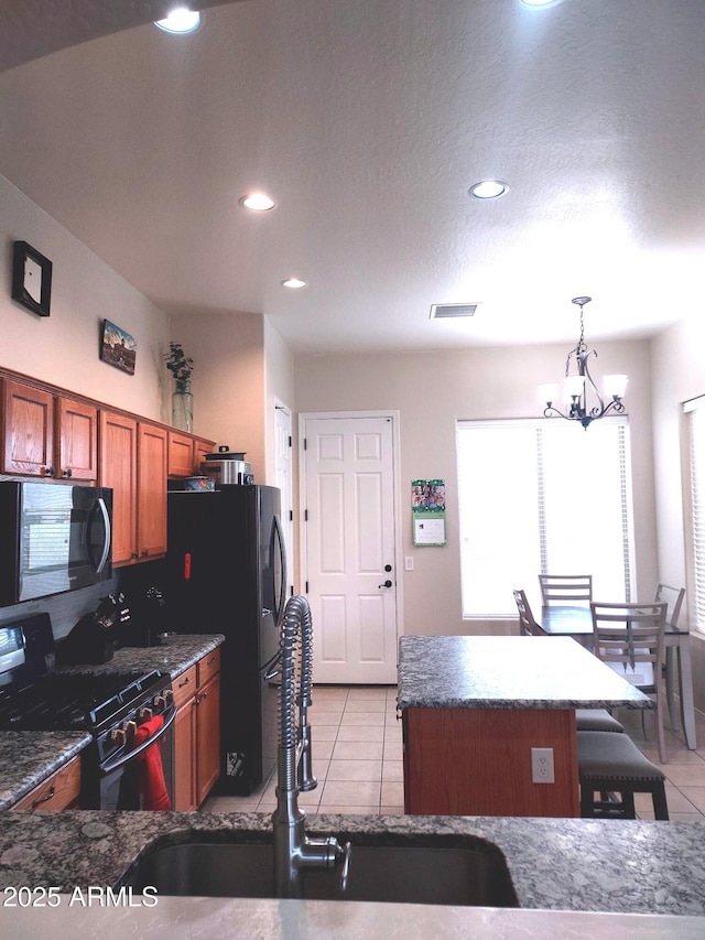 kitchen with visible vents, black appliances, a kitchen island, light tile patterned flooring, and a sink