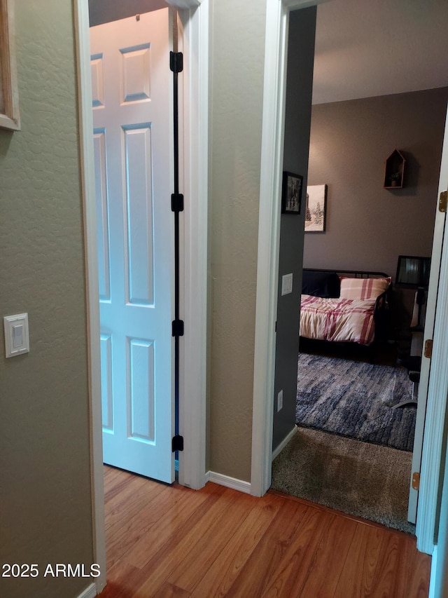 hall with a textured wall, baseboards, and wood finished floors