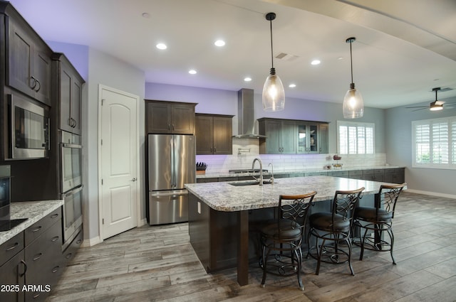 18175 W Highland Ave, Goodyear, AZ 85395 - kitchen featuring backsplash, stainless steel appliances, light wood finished floors, and wall chimney exhaust hood
