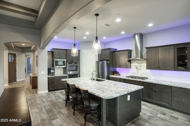 18175 W Highland Ave, Goodyear, AZ 85395 - kitchen with wall chimney range hood, arched walkways, stainless steel appliances, decorative backsplash, and light wood-type flooring