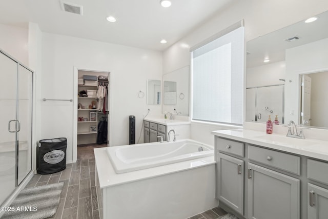 bathroom with visible vents, a sink, a walk in closet, a shower stall, and a bath