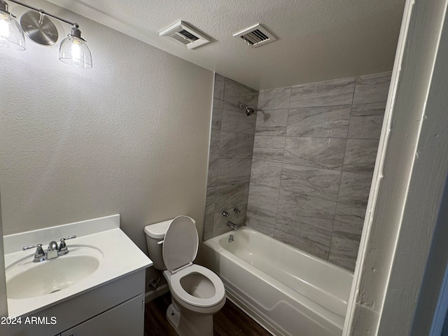 full bathroom with a textured ceiling, tiled shower / bath combo, vanity, and toilet