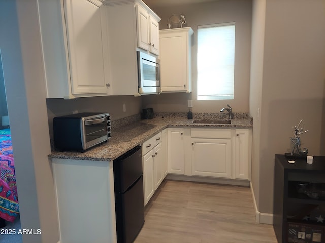 kitchen with stainless steel microwave, sink, light hardwood / wood-style flooring, fridge, and white cabinetry