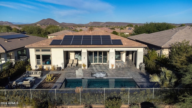 rear view of property with a mountain view, solar panels, a patio, and a fenced in pool