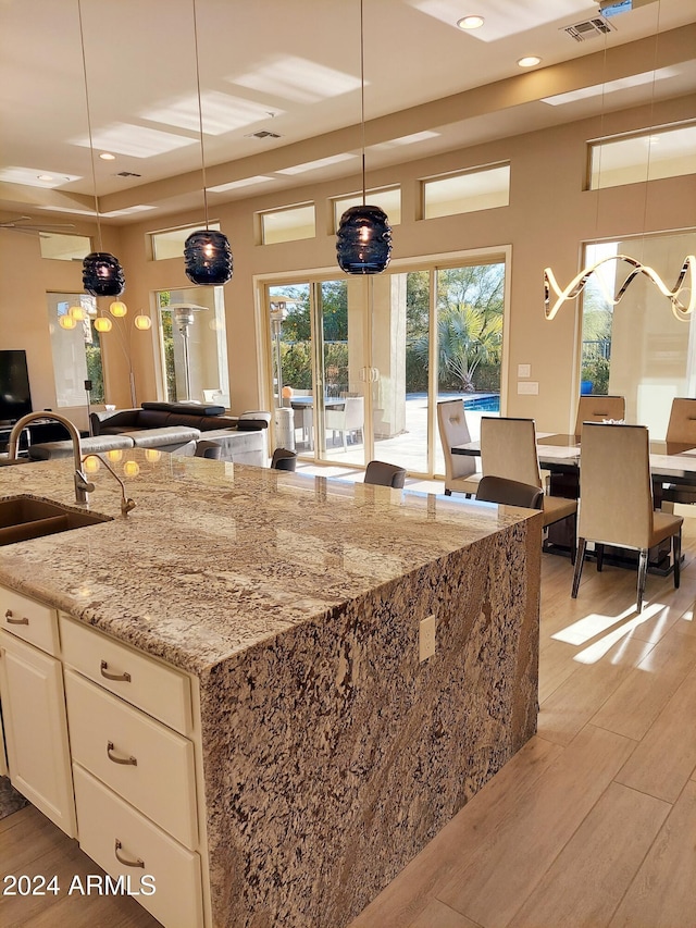 kitchen featuring light stone counters, a tray ceiling, sink, hanging light fixtures, and an island with sink