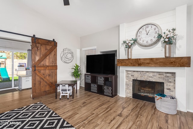 living room featuring hardwood / wood-style floors, a barn door, a brick fireplace, and lofted ceiling