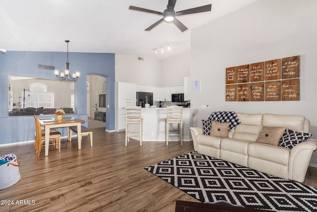 living room with ceiling fan with notable chandelier, rail lighting, high vaulted ceiling, and dark wood-type flooring