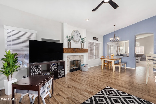 living room with ceiling fan with notable chandelier, a stone fireplace, lofted ceiling, and light hardwood / wood-style flooring