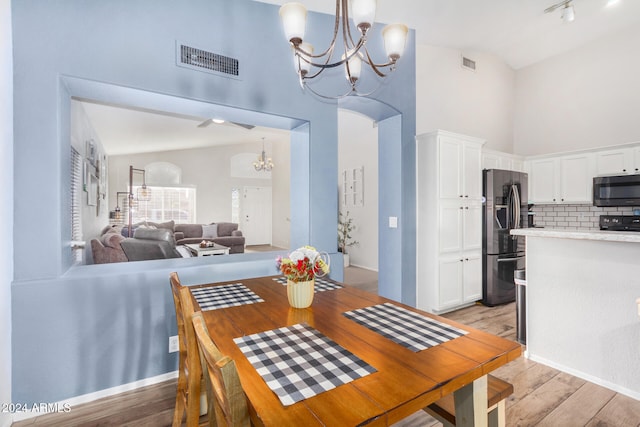 dining space with light hardwood / wood-style flooring, high vaulted ceiling, and ceiling fan with notable chandelier