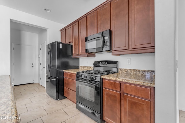 kitchen featuring light stone countertops, light tile patterned floors, and black appliances