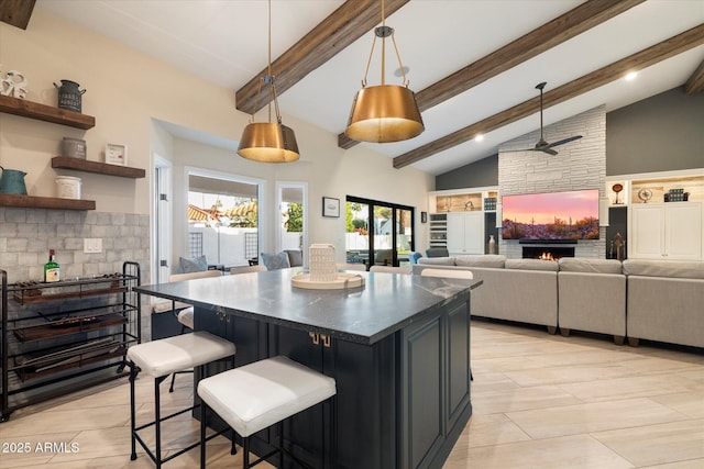 kitchen featuring high vaulted ceiling, a ceiling fan, a kitchen island, dark countertops, and a lit fireplace