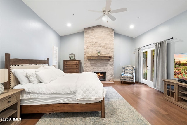 bedroom with access to outside, wood finished floors, a stone fireplace, lofted ceiling, and ceiling fan