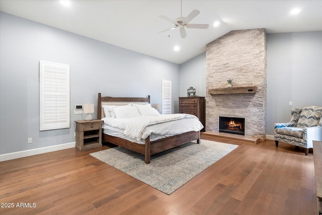 bedroom with high vaulted ceiling, wood finished floors, a fireplace, baseboards, and ceiling fan