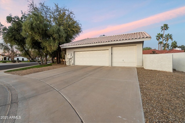 view of front facade with stucco siding, a tiled roof, driveway, and fence