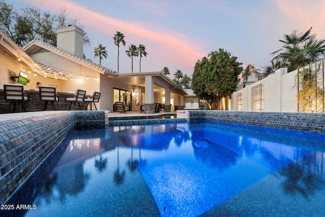 pool at dusk featuring a patio, an outdoor pool, and outdoor dry bar