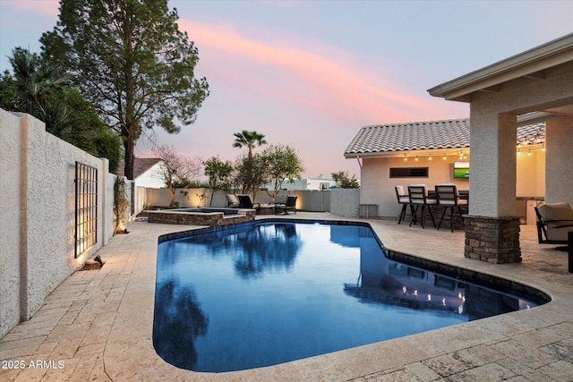 pool at dusk with a fenced backyard, a pool with connected hot tub, outdoor dry bar, and a patio area